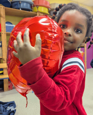 Une petite fille fait un calin à un ballon de baudruche en forme de coeur