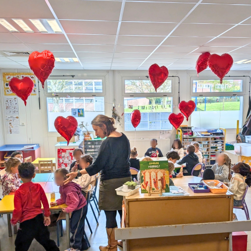 Des enfants d'une classe de maternelle fabriquent des objets avec des ballons de baudruche en forme de coeur qui flottent dans le ciel.