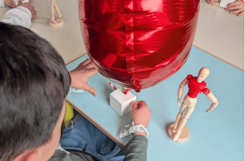 Un enfant fabrique une machine avec un ballon de baudruche en forme de coeur et un petit personnage en forme de Toby