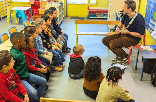 Un comédien joue du ukulélé et chante la chanson de Toby devant une classe de maternelle